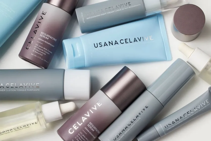 USANA Celavive 系列保養品產品實拍圖,包含淨透煥膚精華(Resurfacing Serum)、水潤調理美顏露、煥顏光采護膚油及眼霜等多款灰色與藍色系瓶身產品,展現專業且純淨的品牌形象。